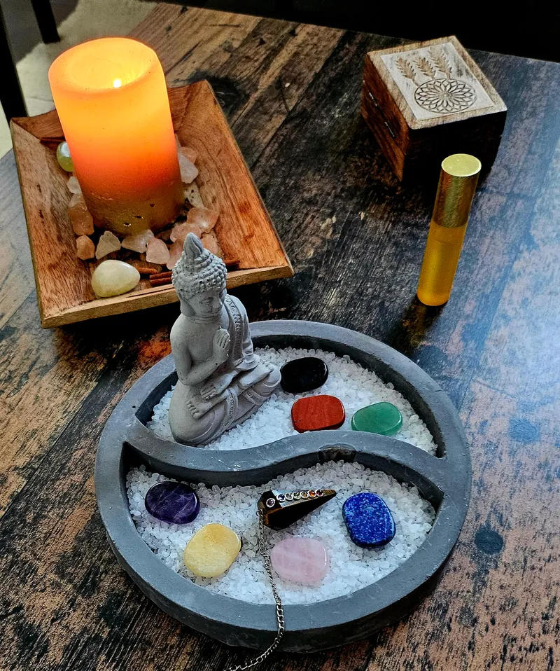 Zen-Garten mit Buddha-Statue, bunten Chakra-Steinen, Kerze und ätherischem Öl